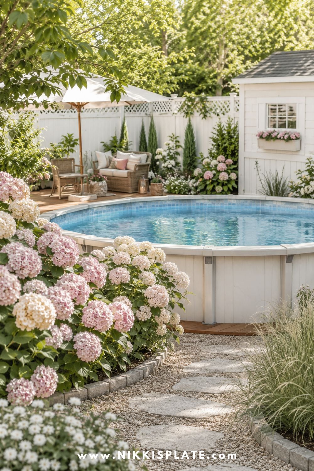 Above ground pool surrounded by pink and white hydrangeas, soft ornamental grasses, stone edging, and a bright backyard seating area.