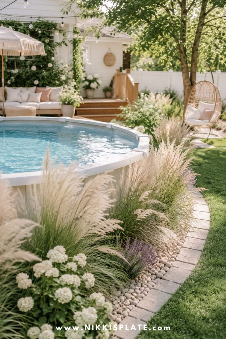 Above ground pool with soft ornamental grasses, white flowers, river rock edging, and a cozy backyard lounge area.