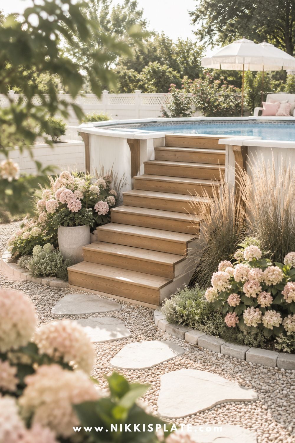 Tall above ground pool with wood steps leading to the pool ledge, soft flowers, ornamental grasses, gravel edging, and stepping stones.