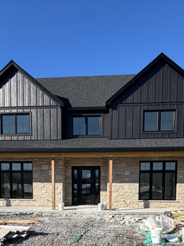 Modern farmhouse exterior with limestone front, black board and batten siding, black windows, and black roof shingles on our rural Ontario custom home build.