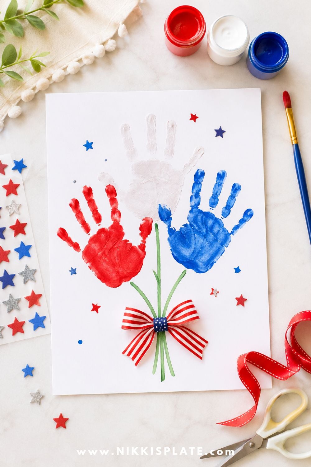 Patriotic handprint craft for kids with red, white, and blue painted handprints arranged like a bouquet with star stickers and craft supplies