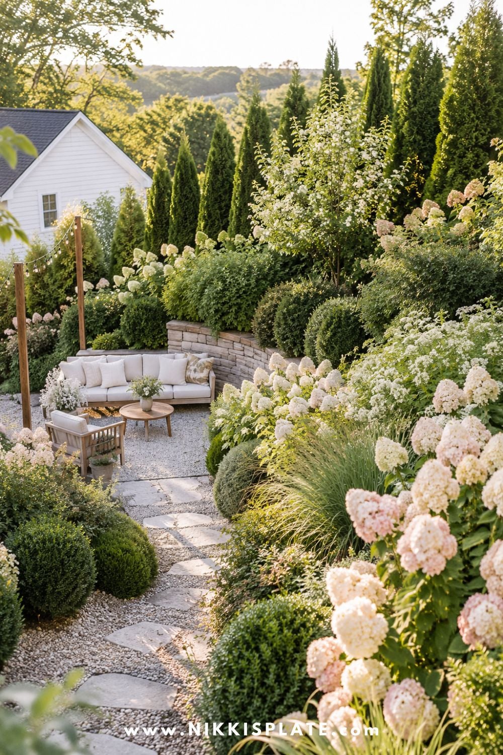 Sloped backyard landscaping with privacy planting along the slope, tall evergreens, hydrangeas, layered shrubs, gravel path, and cozy secluded seating area.