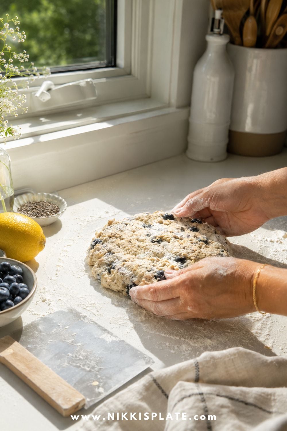 Female hands shaping blueberry chia sourdough scone dough into a round on a lightly floured kitchen counter.