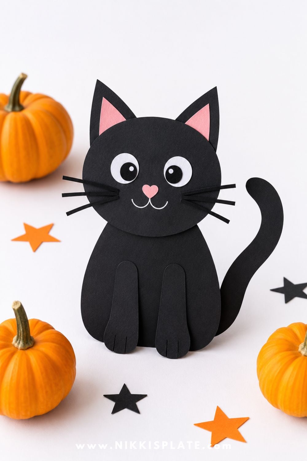 Black construction paper cat craft with tail, whiskers, big friendly eyes, and pink nose for an easy Halloween craft for preschoolers and kids.