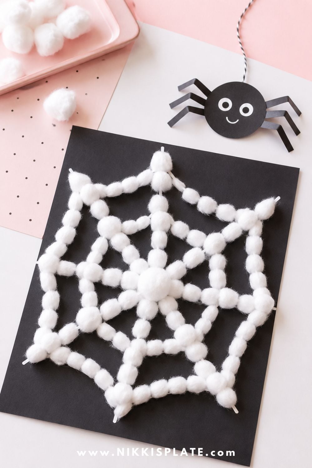 Cotton ball spider web craft on black paper with a cute paper spider for a simple low-mess Halloween craft for toddlers and preschoolers.