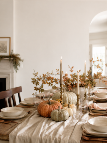 Cozy fall table decor with neutral pumpkins, brass candles, autumn branches and a soft linen runner on a farmhouse dining table.