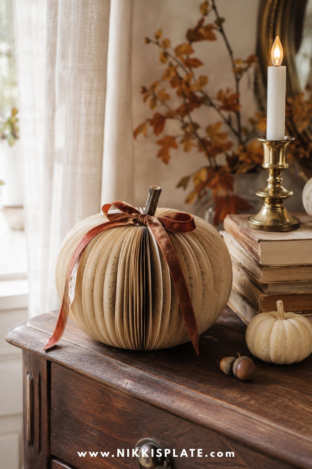 Handmade paperback book pumpkin with softly aged pages, a twig stem and rust velvet ribbon on a vintage wood table.