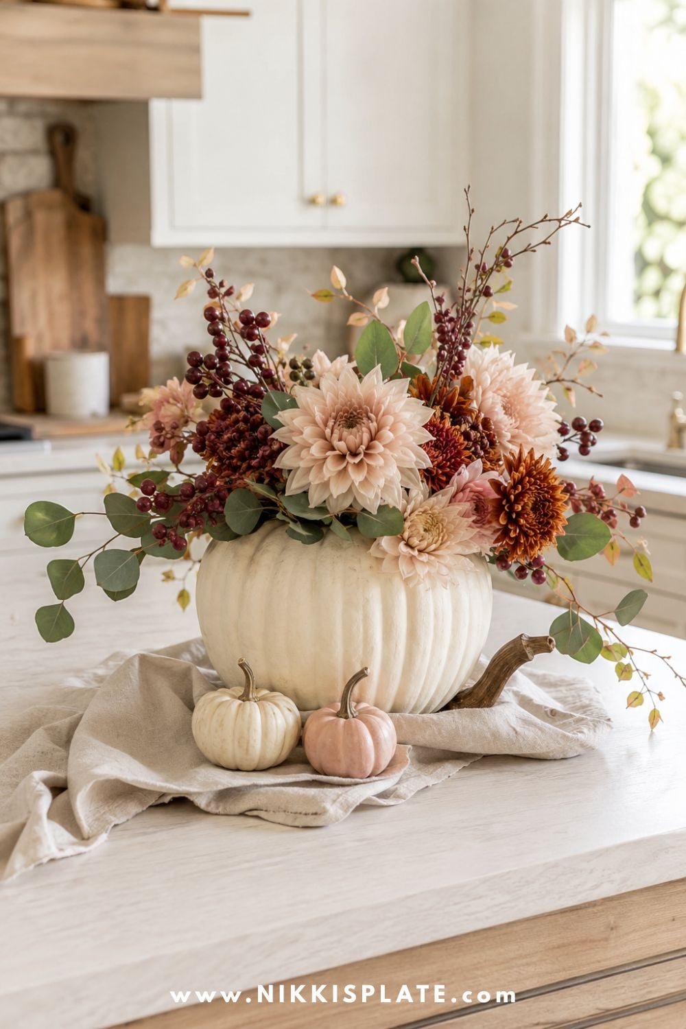 Cream pumpkin vase filled with rust dahlias, burgundy berries, eucalyptus and autumn branches on a farmhouse kitchen island.