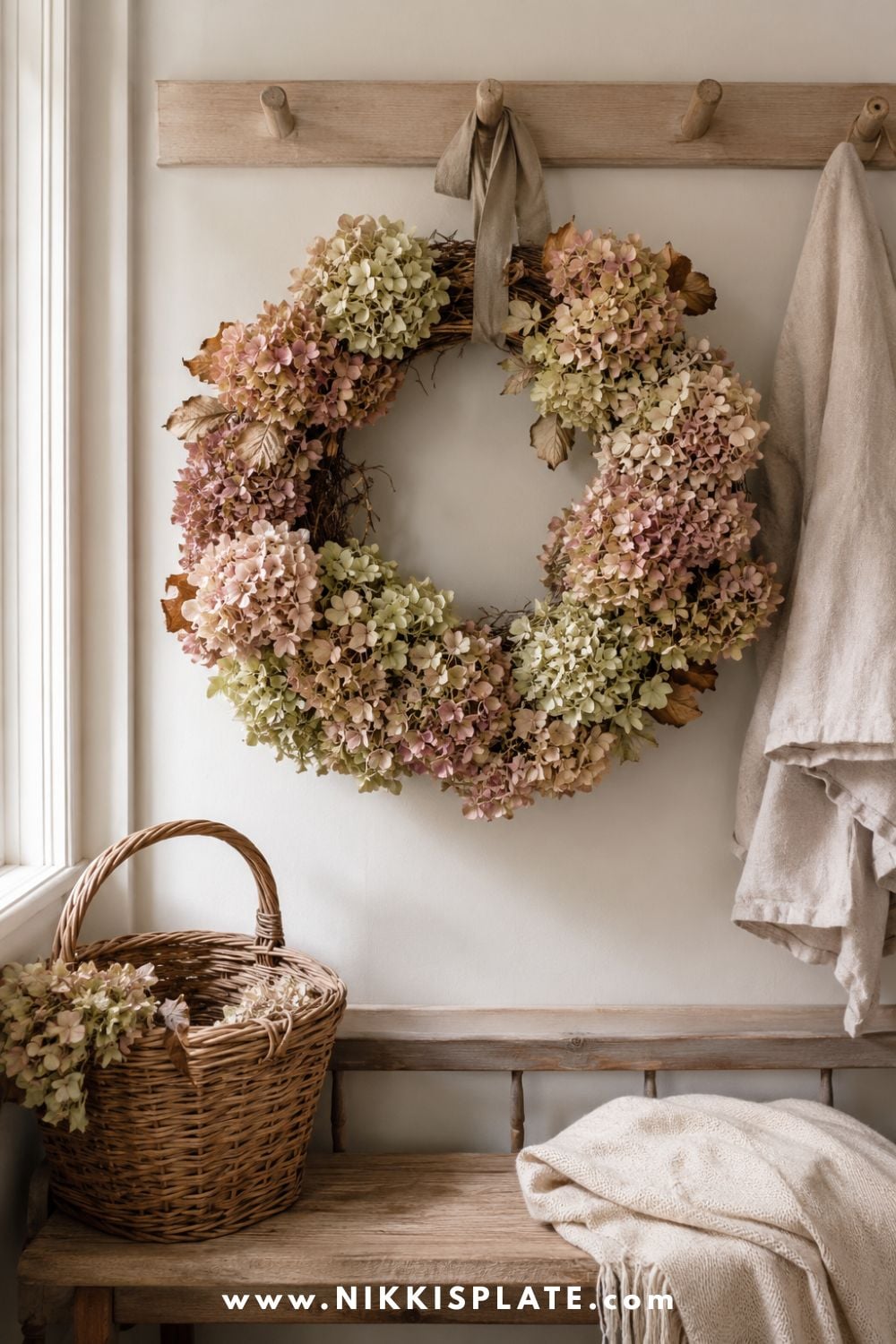 Full dried hydrangea wreath in antique blush, muted green and cream hanging above a farmhouse mudroom bench.