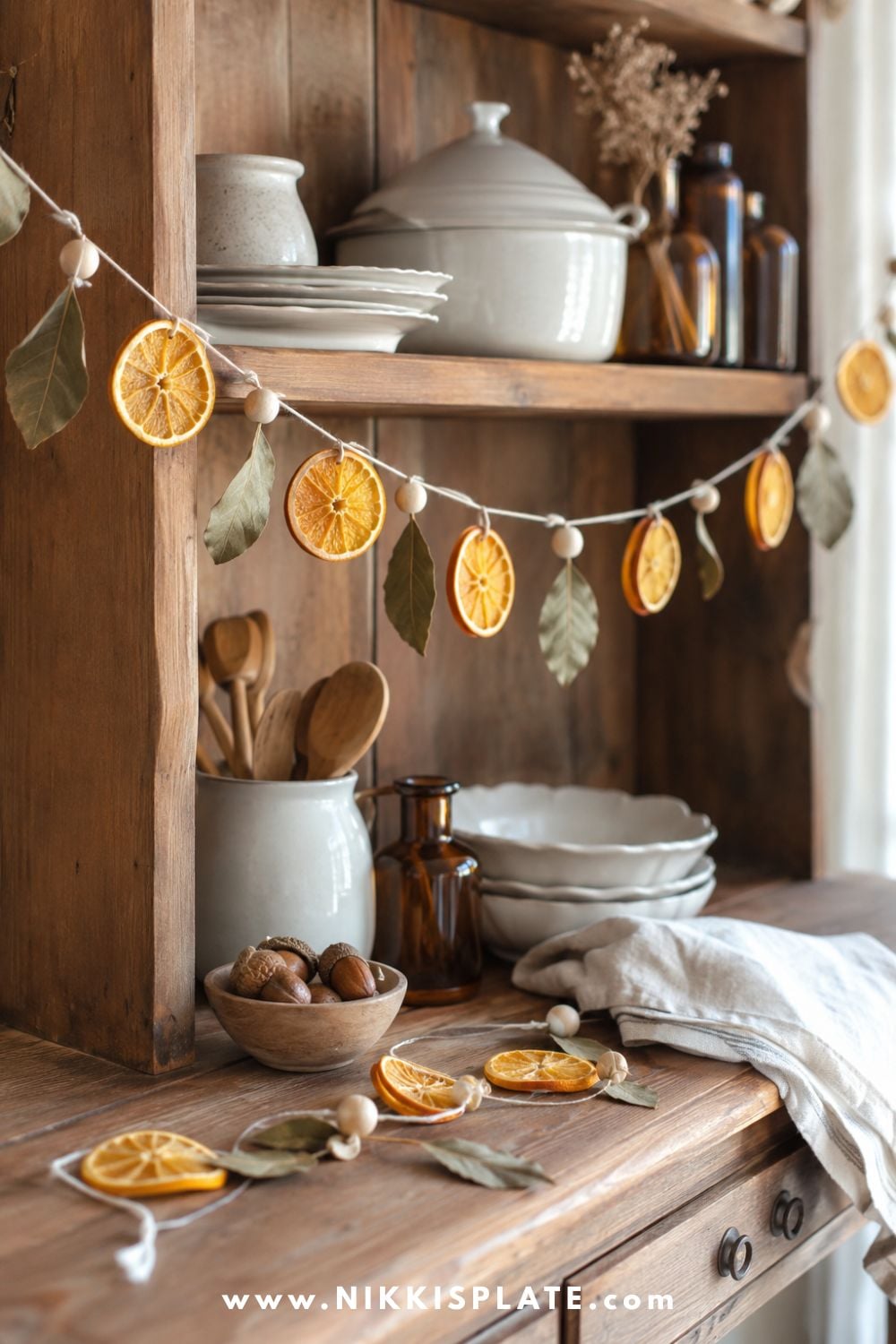Dried orange and bay leaf garland with natural wood beads draped across a warm wood farmhouse kitchen hutch.