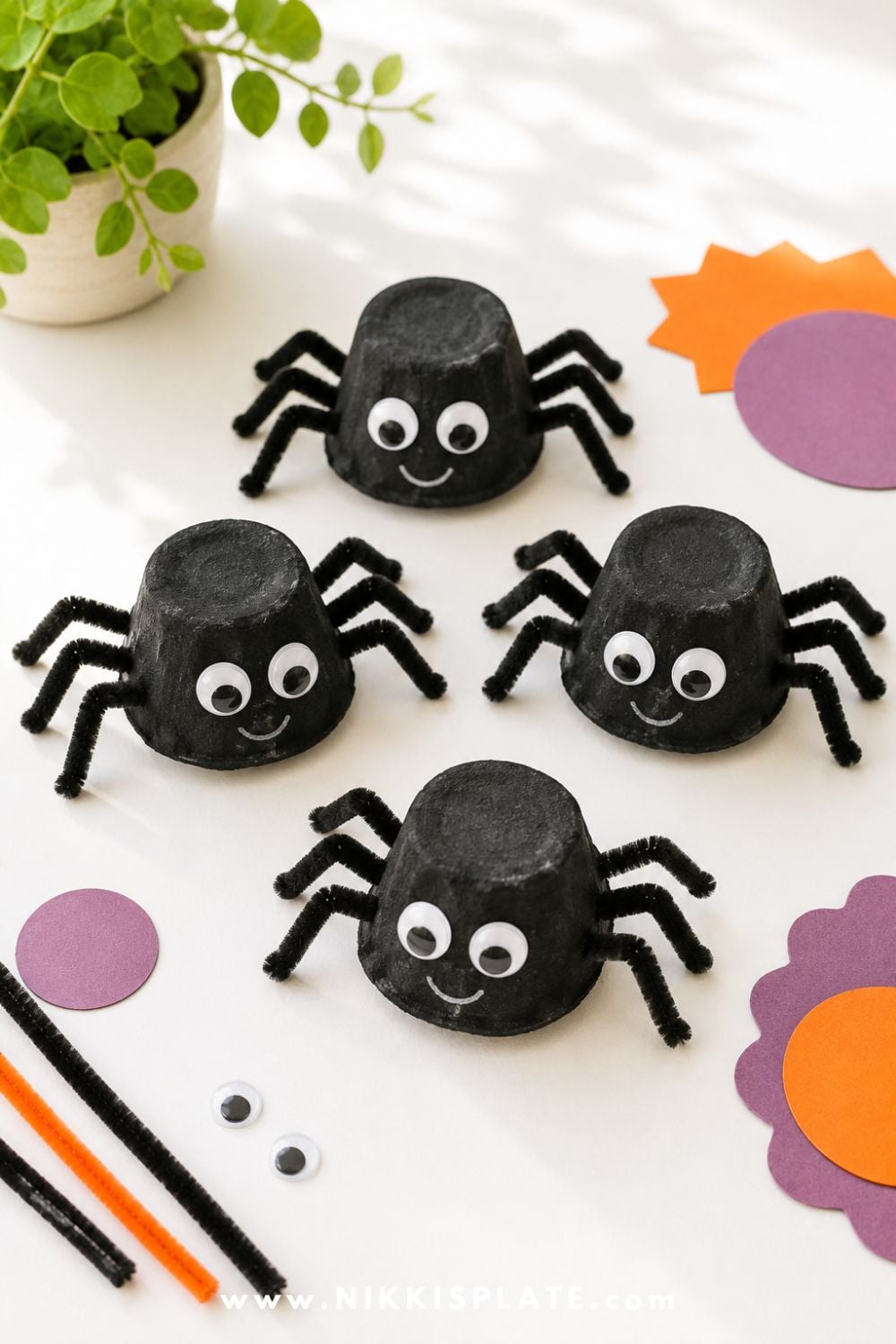 Black egg carton spider crafts with pipe cleaner legs and googly eyes, arranged on a bright table for a cute recycled Halloween craft for kids.