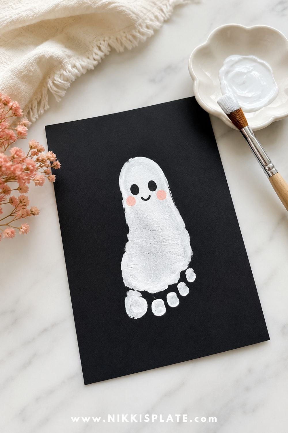 White ghost footprint keepsake craft on black paper with a cute ghost face, styled as a sweet Halloween keepsake craft for kids.