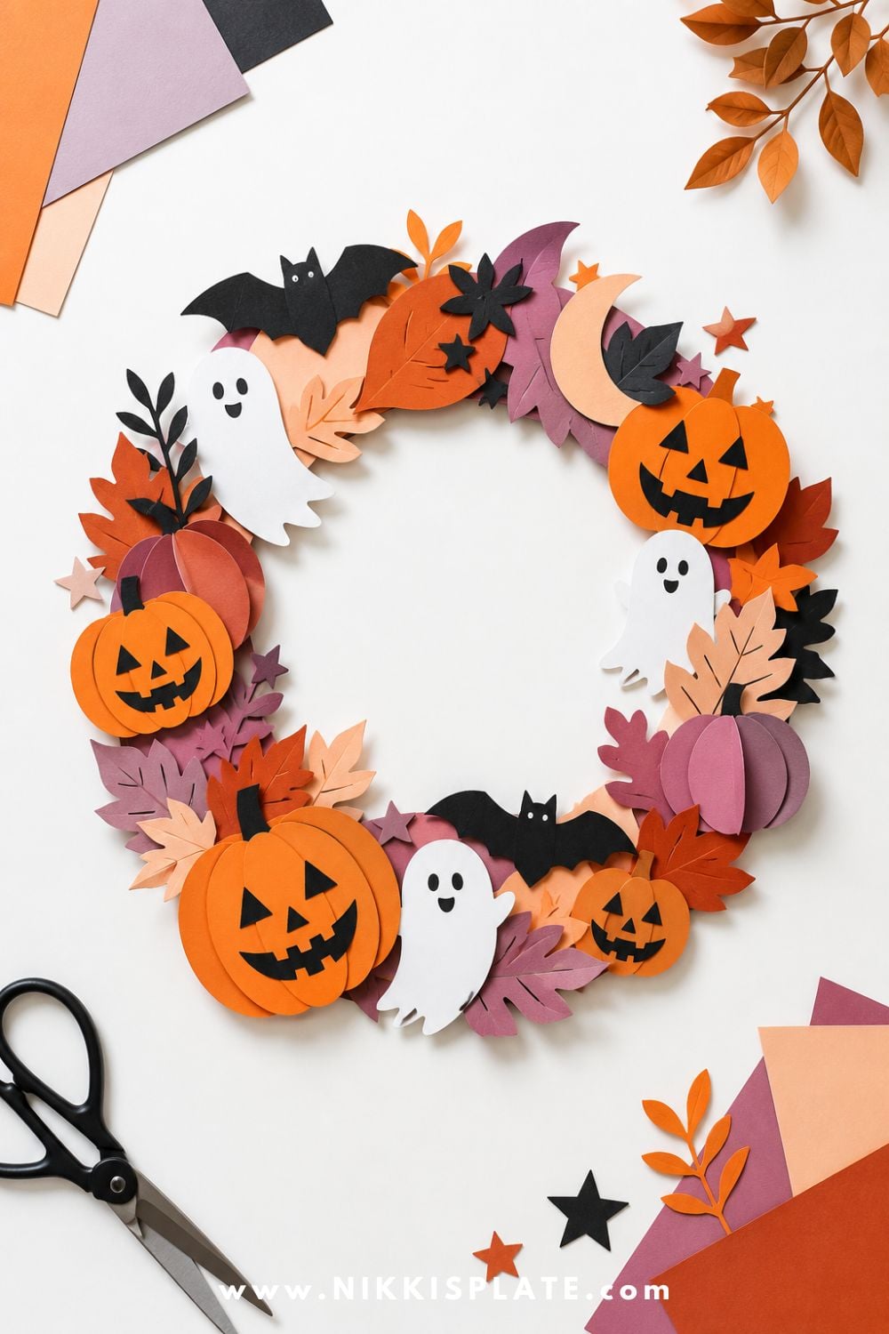Paper Halloween wreath decorated with pumpkins, ghosts, bats, leaves, and stars in soft seasonal colors for a cute Halloween craft for kids.
