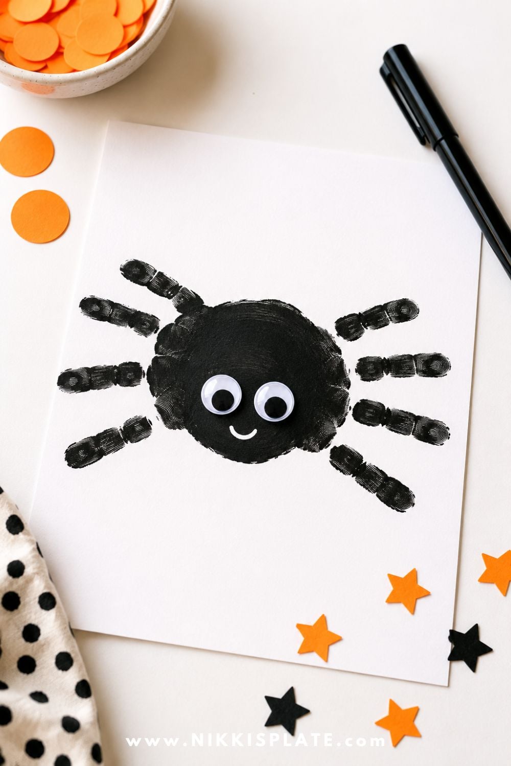 Black handprint spider craft on white paper with googly eyes and a friendly smile, perfect for an easy Halloween keepsake craft for kids.
