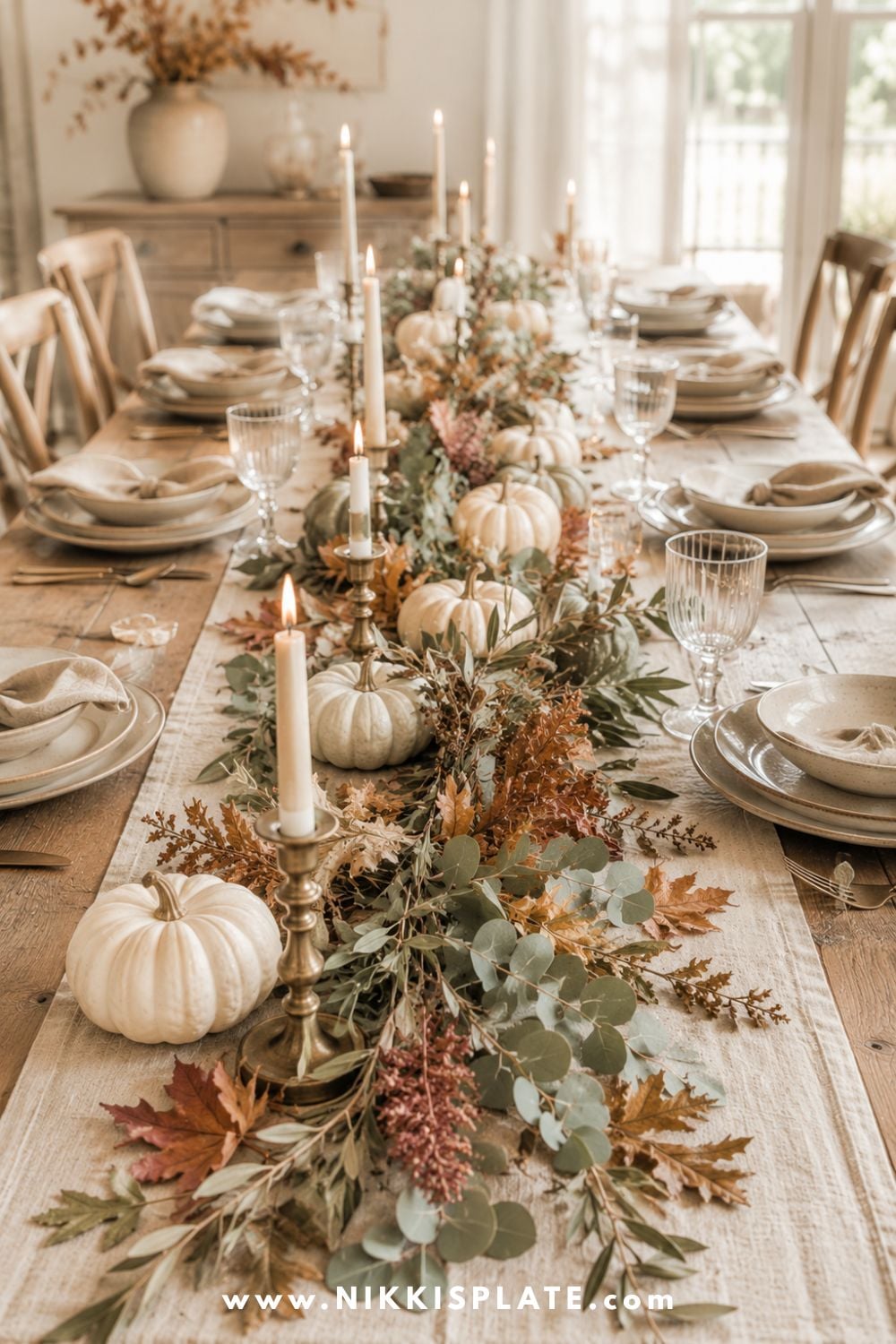 Loose fall garland with eucalyptus, maple leaves, cream pumpkins and brass candles arranged down a wooden table.