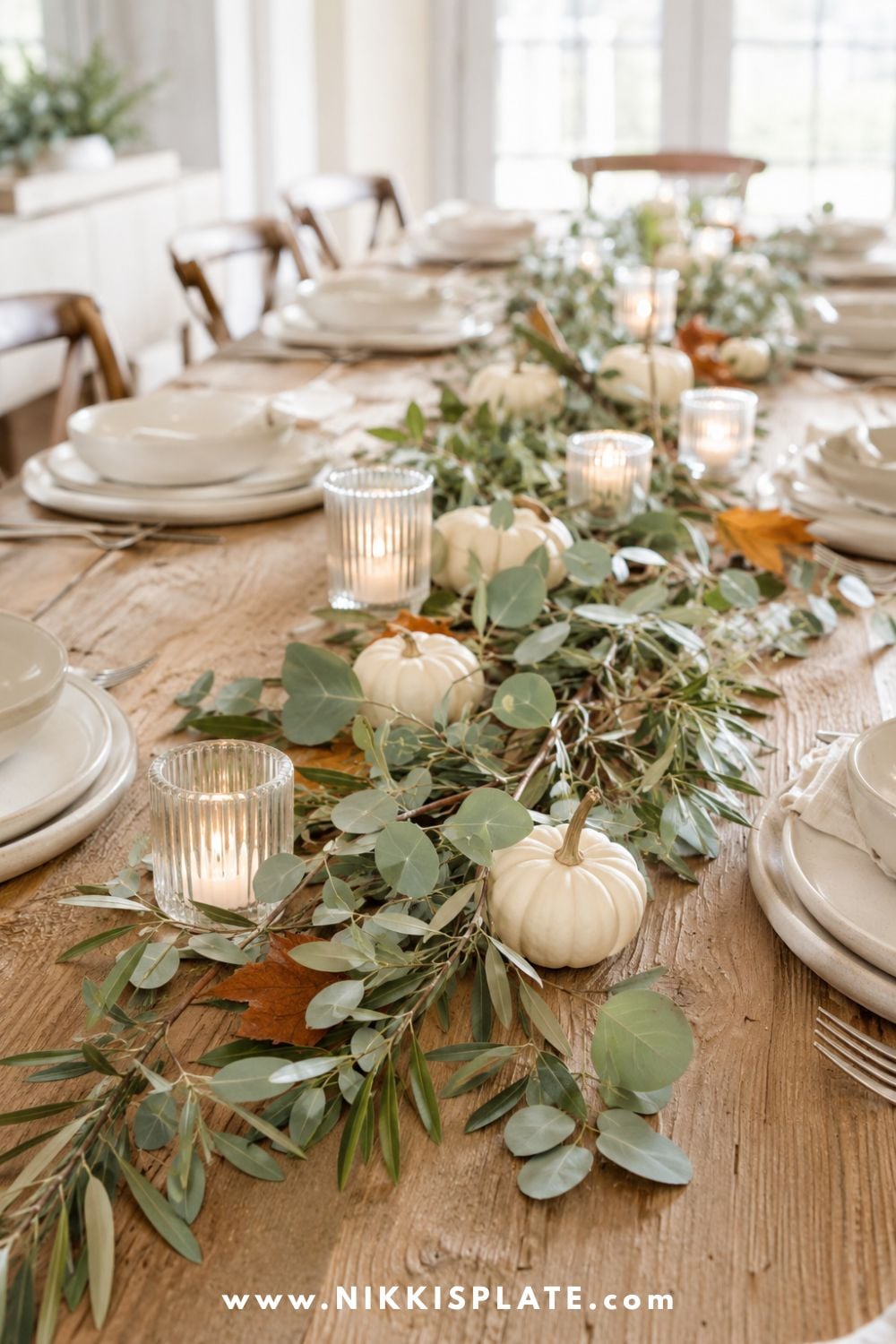 Low fall table centerpiece with eucalyptus, olive branches, votive candles and small cream pumpkins.