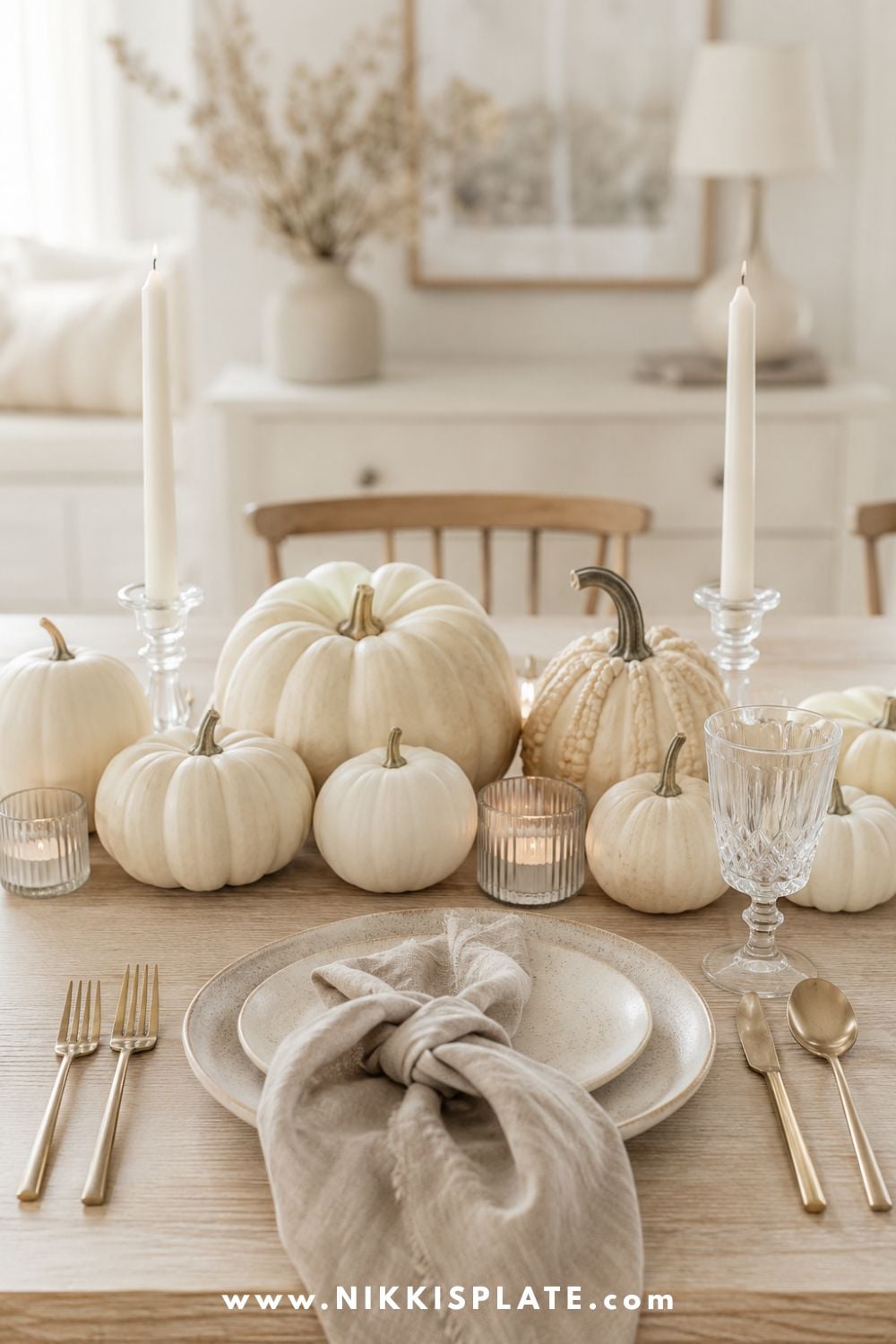 Modern fall table decor in an ivory palette with neutral pumpkins, cream stoneware and clear candleholders.
