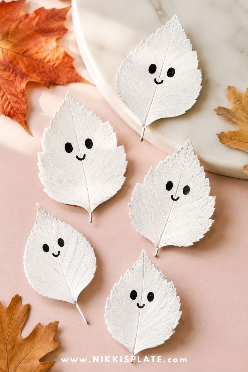 White painted fall leaves turned into cute ghost crafts with friendly faces for a simple nature-inspired Halloween craft for kids.