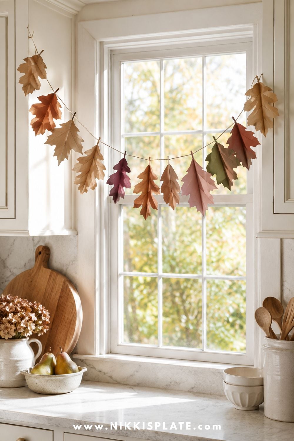Kraft paper leaf garland with hand-painted rust, olive and burgundy leaves hanging across a bright farmhouse kitchen window.