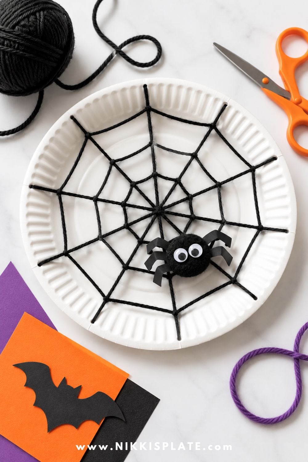 Paper plate spider web craft with white yarn woven across the plate and a cute paper spider for an easy Halloween craft for kids.