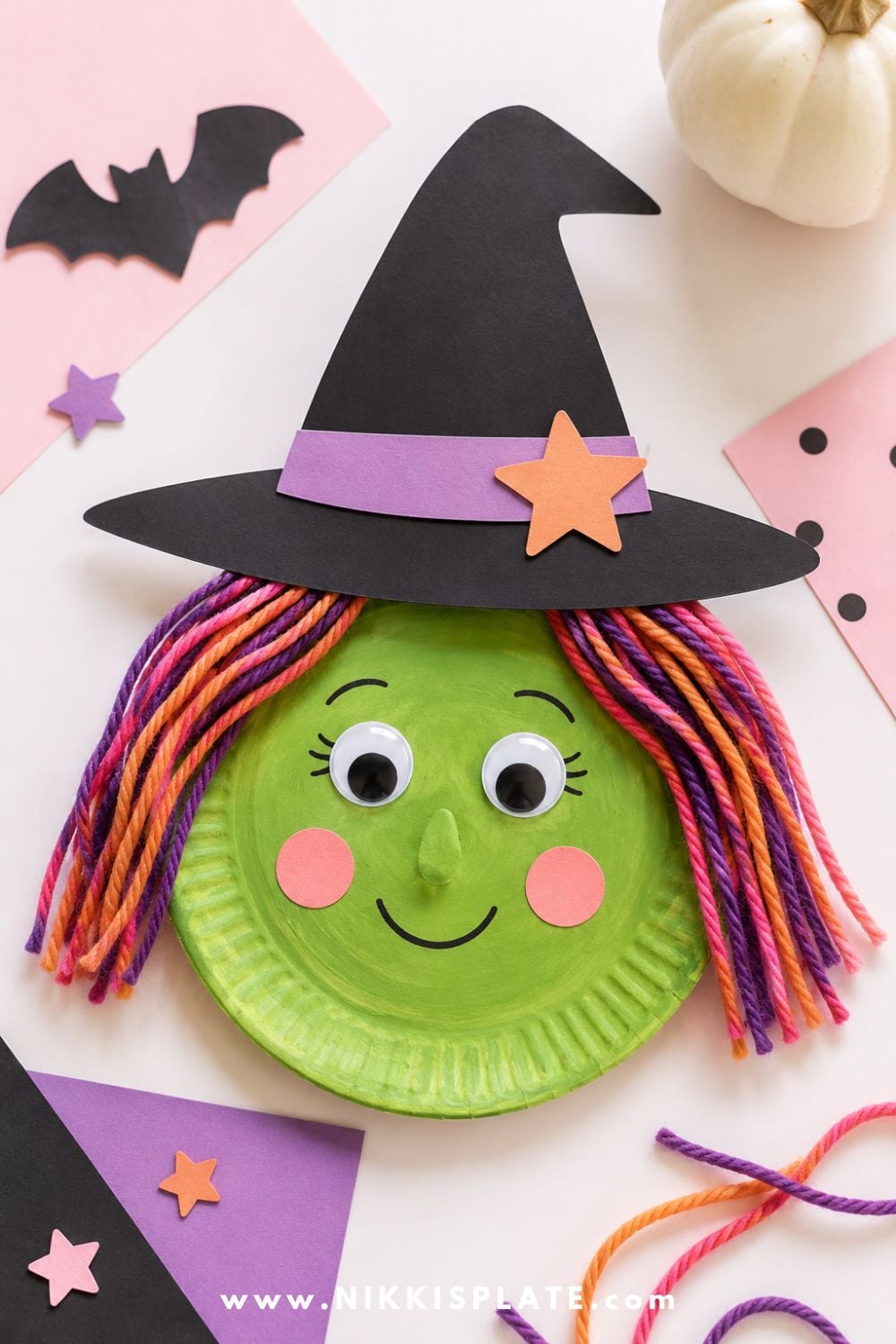 Friendly paper plate witch craft with green face, paper hat, yarn hair, and googly eyes for a cute preschool Halloween craft idea.