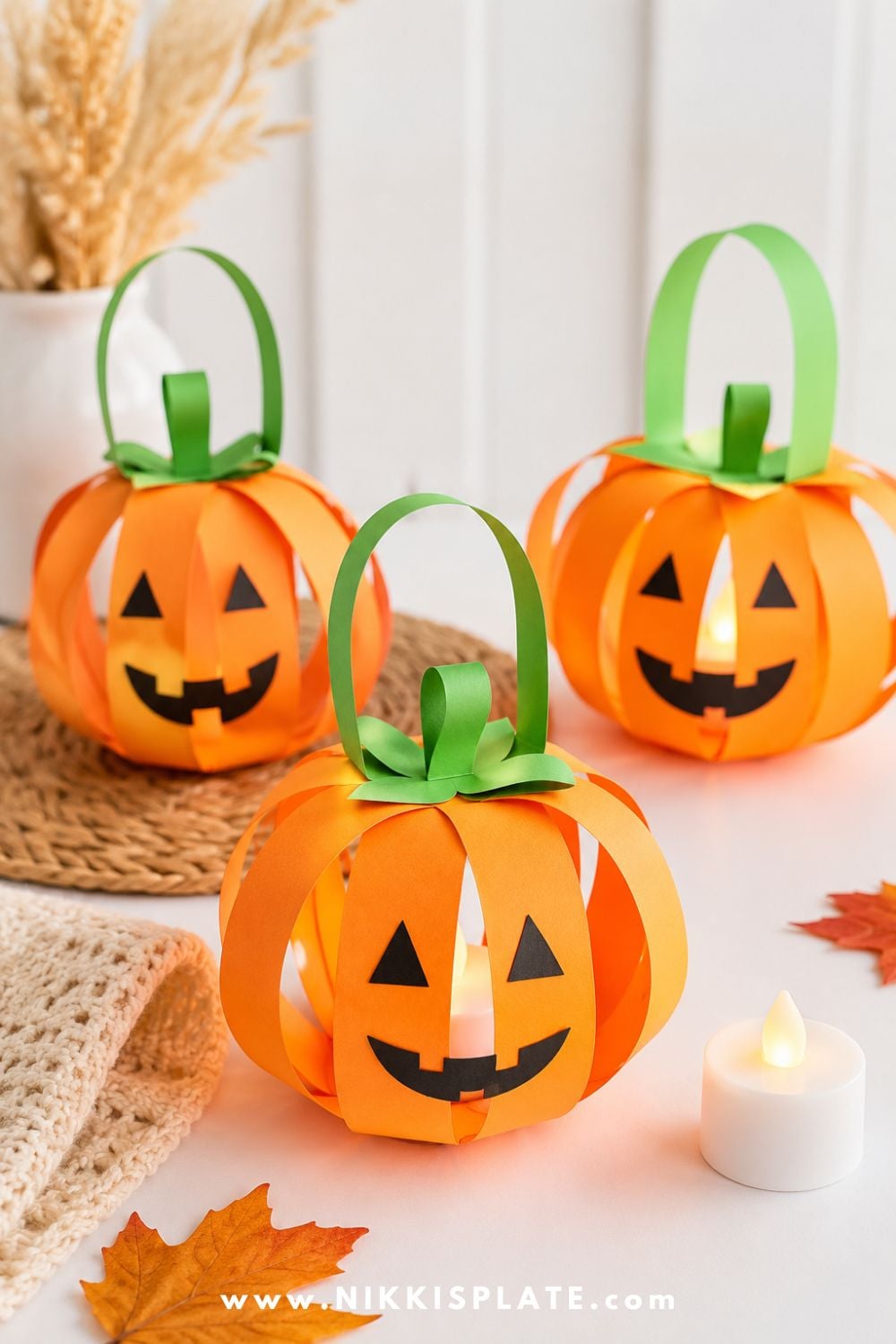 Orange paper pumpkin lantern craft with green handle and stem, styled with a battery tea light for a cute Halloween craft for kids.
