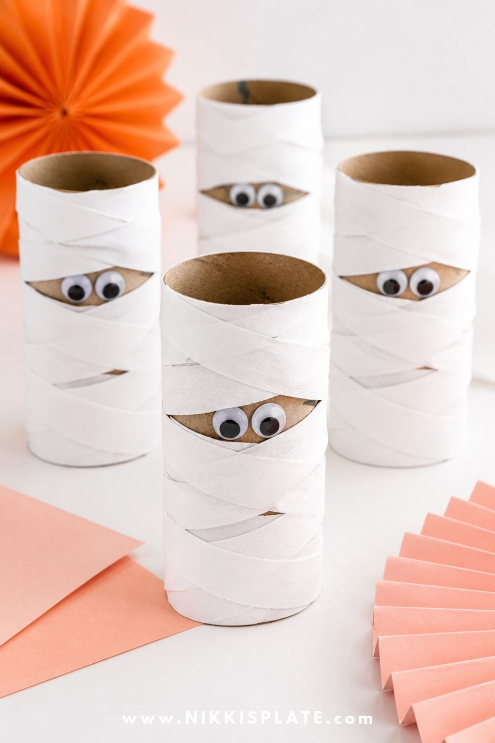 Cardboard paper roll mummy craft wrapped in white paper strips with googly eyes peeking out for a cute Halloween craft for kids.