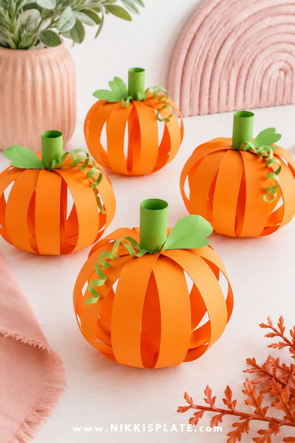 Three-dimensional orange paper strip pumpkin crafts with green stems and curly vines for a cute Halloween craft for kids.