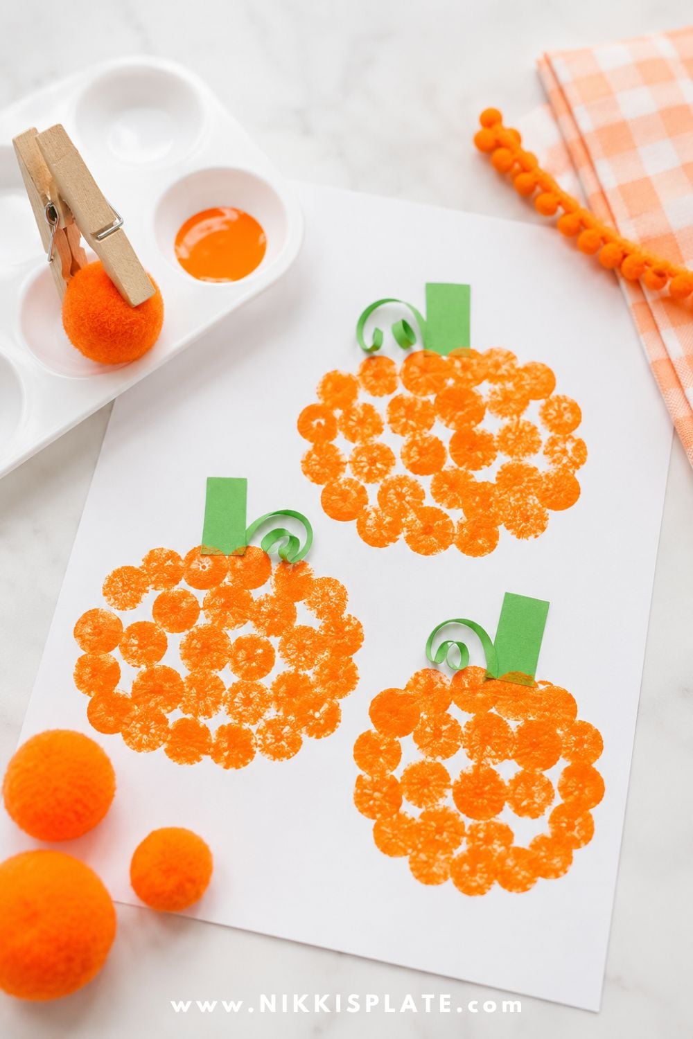 Pom pom stamped pumpkin painting with orange paint and green stems for a cute Halloween craft and sensory painting activity for toddlers.