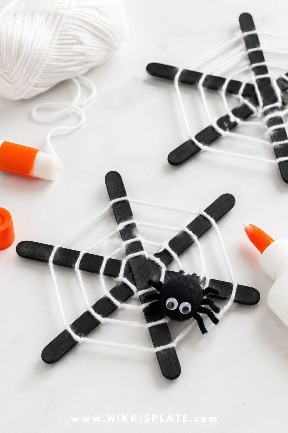 Popsicle stick spider web craft wrapped with white yarn and finished with a cute pom pom spider for an easy preschool Halloween craft.