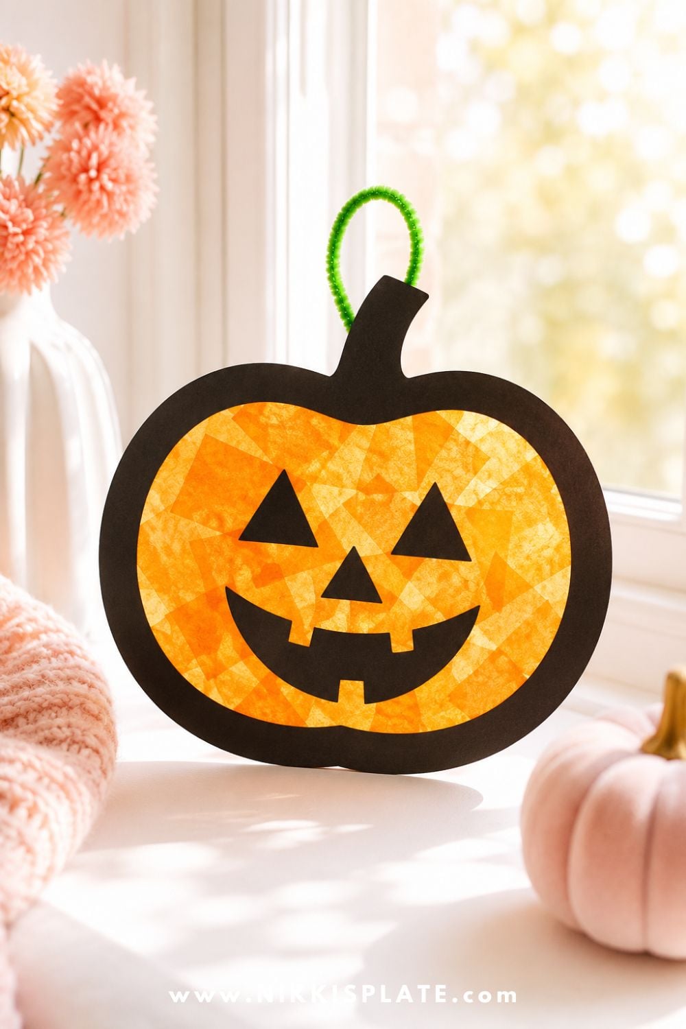 Orange tissue paper pumpkin sun catcher craft with black outline glowing in soft window light for a pretty Halloween craft for kids.