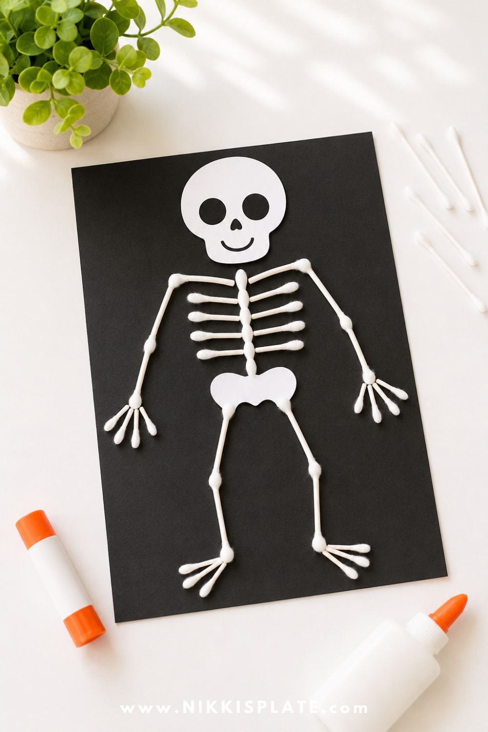 Kid-friendly q-tip skeleton craft on black paper with a simple paper skull face, perfect for an easy Halloween craft and learning activity for kids.