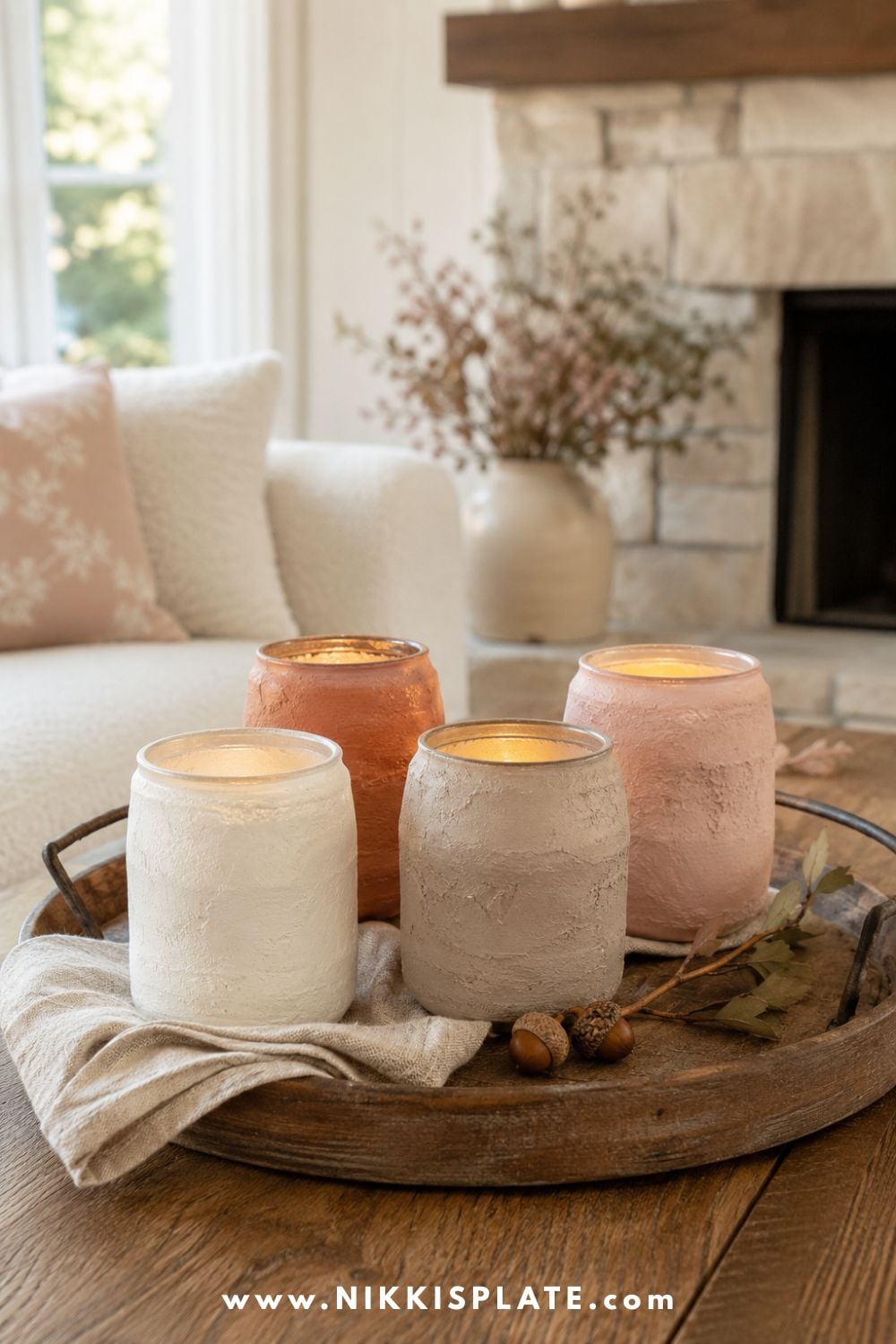 Handmade textured candle holders in cream, taupe, terracotta and blush displayed on a rustic wood coffee table.