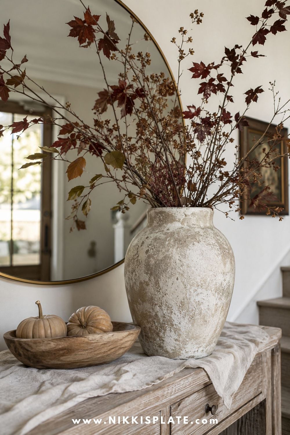 Thrifted vase with a textured limestone finish filled with dramatic burgundy and olive autumn branches on an entryway table.