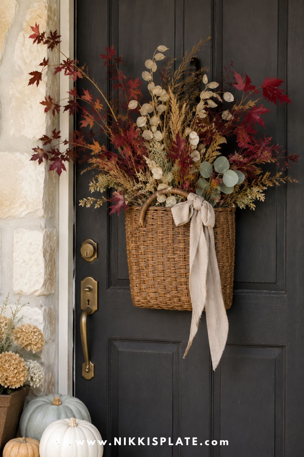 Vintage wall basket filled with burgundy maple branches, eucalyptus, seed pods and dried grasses on a dark farmhouse door.