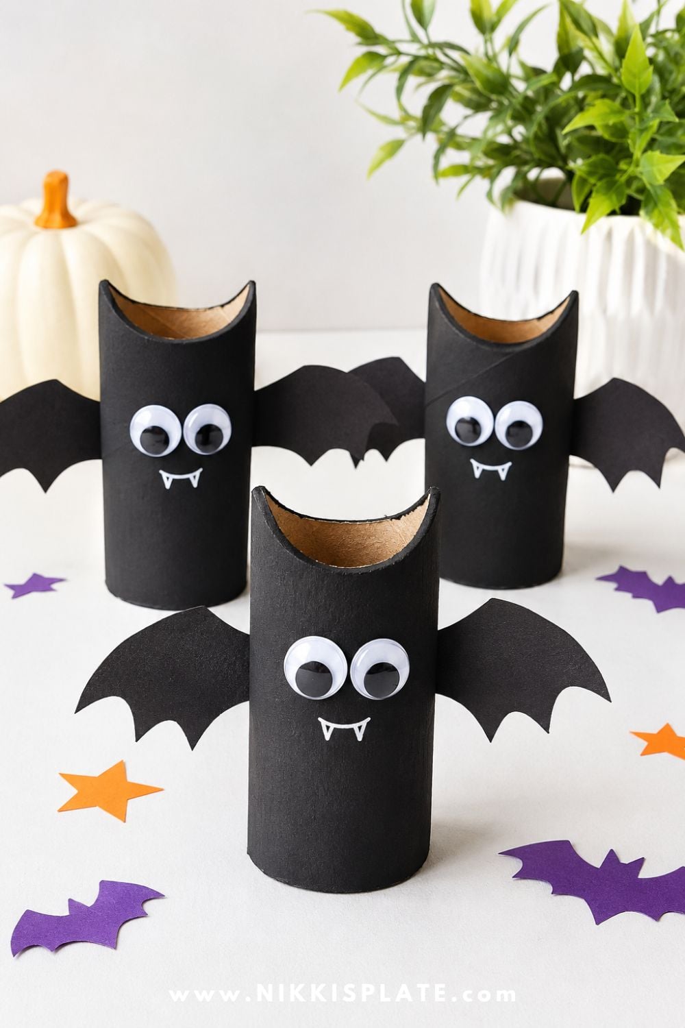 Black toilet paper roll bat craft with paper wings and googly eyes, displayed on a bright white background for an easy recycled Halloween craft for kids.