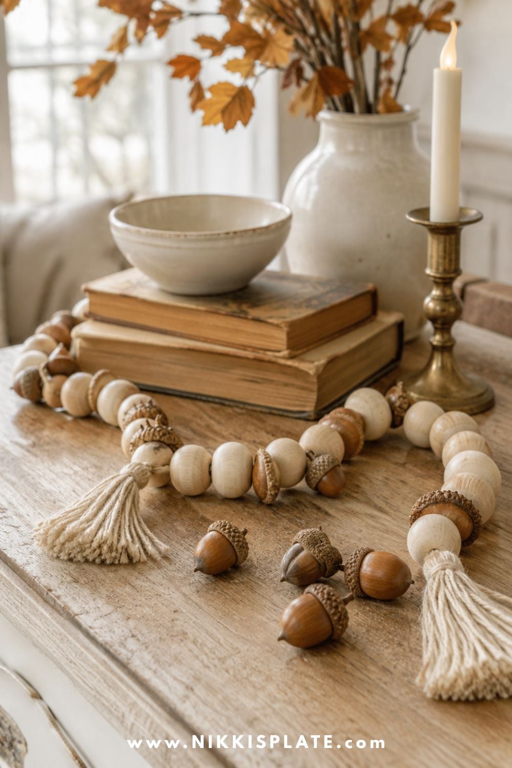 Natural wood bead and acorn garland with cream tassels styled around vintage books and fall decor on a console table.