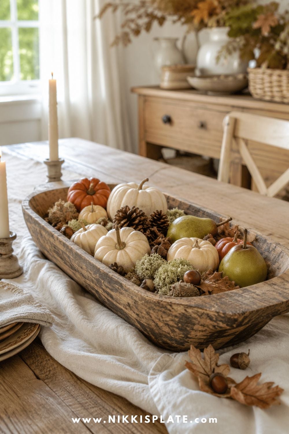 Wooden dough bowl fall centerpiece filled with mini pumpkins, pinecones, acorns, moss and autumn leaves.