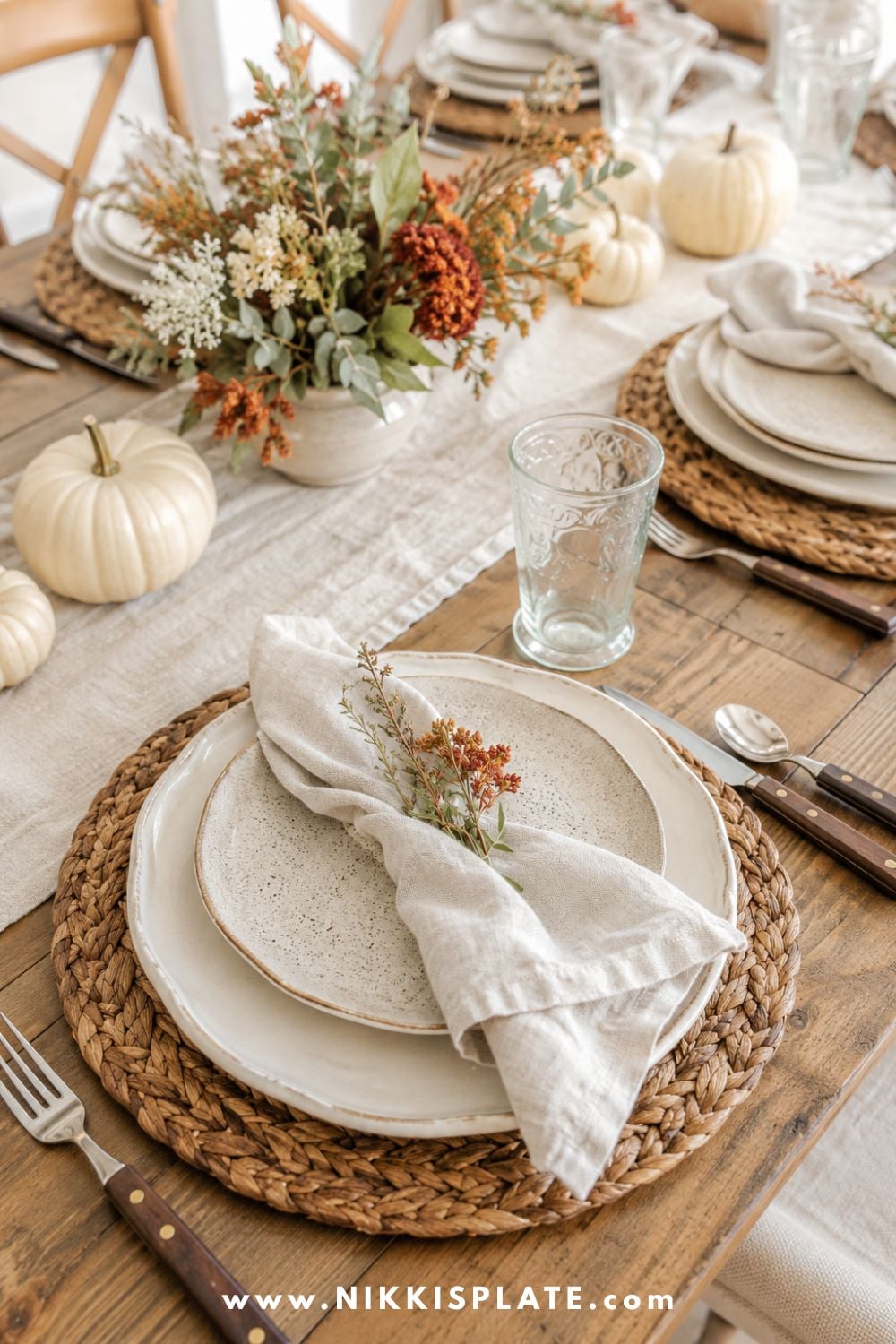 Layered fall table setting with woven placemats, cream stoneware dishes, linen napkins and wood-handled flatware.