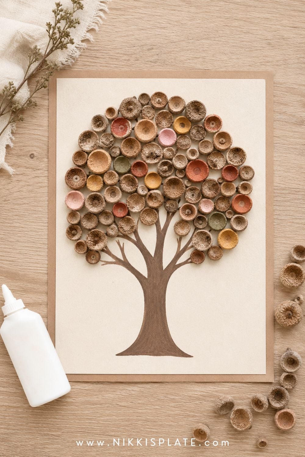 Acorn cap art showing an autumn tree filled with natural and painted acorn caps on cream cardboard.