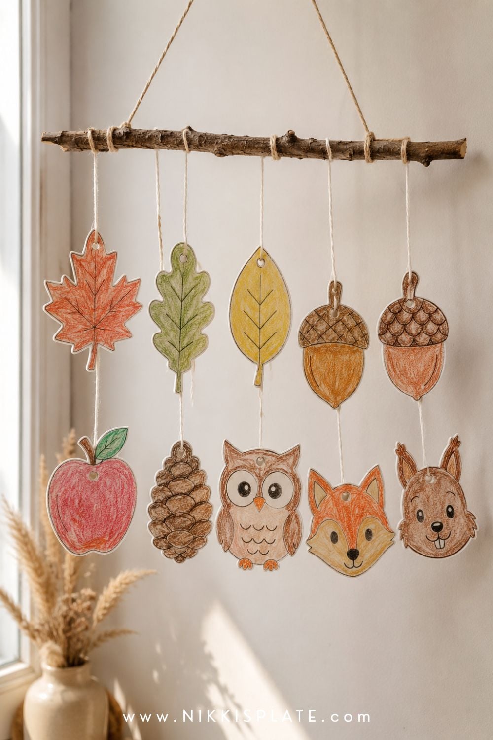 Printable autumn nature mobile with child-coloured leaves, acorns, woodland animals and a paper pinecone hanging from a twig.