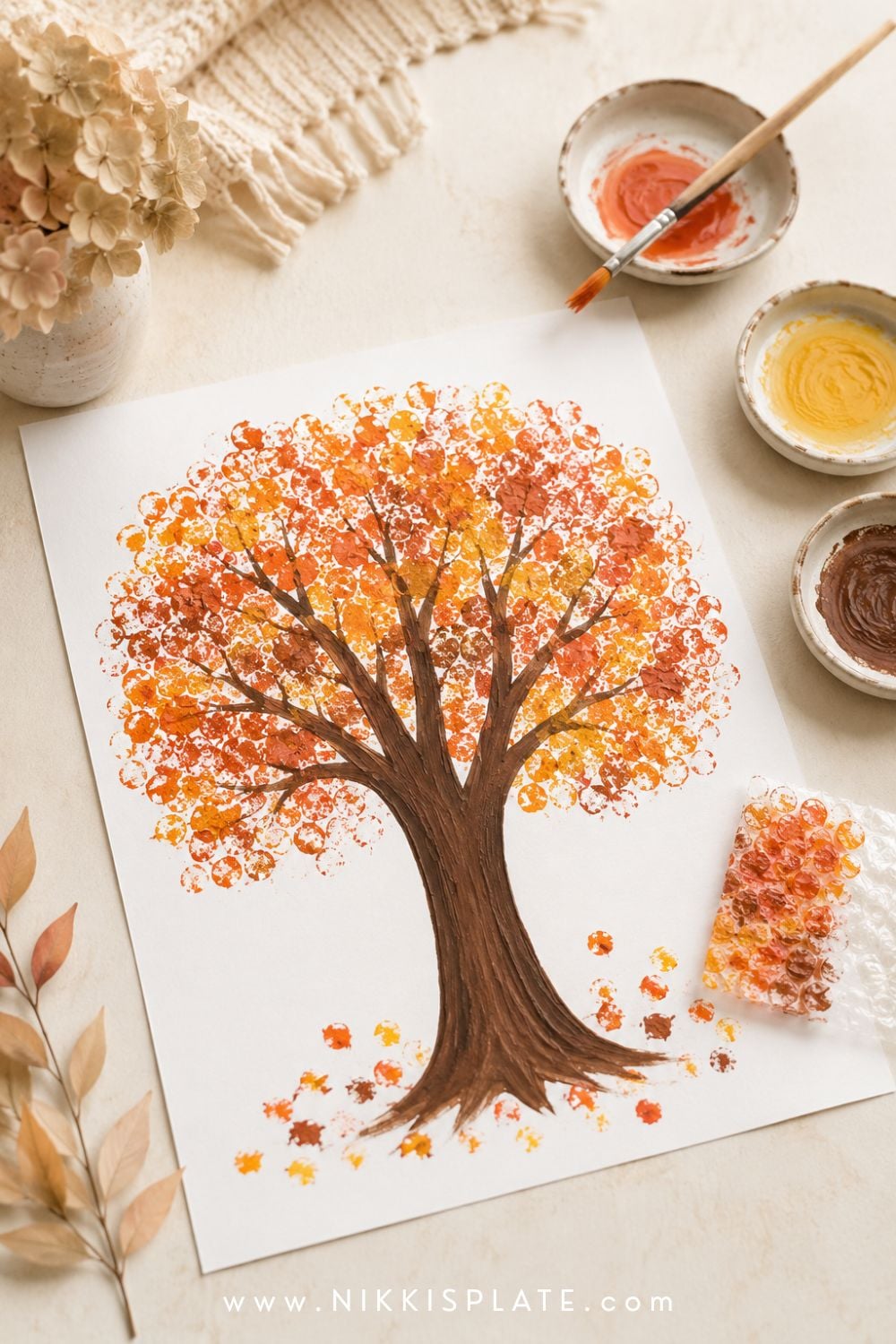 Bubble wrap fall tree painting for kids with a textured orange, red and golden canopy above a brown trunk.