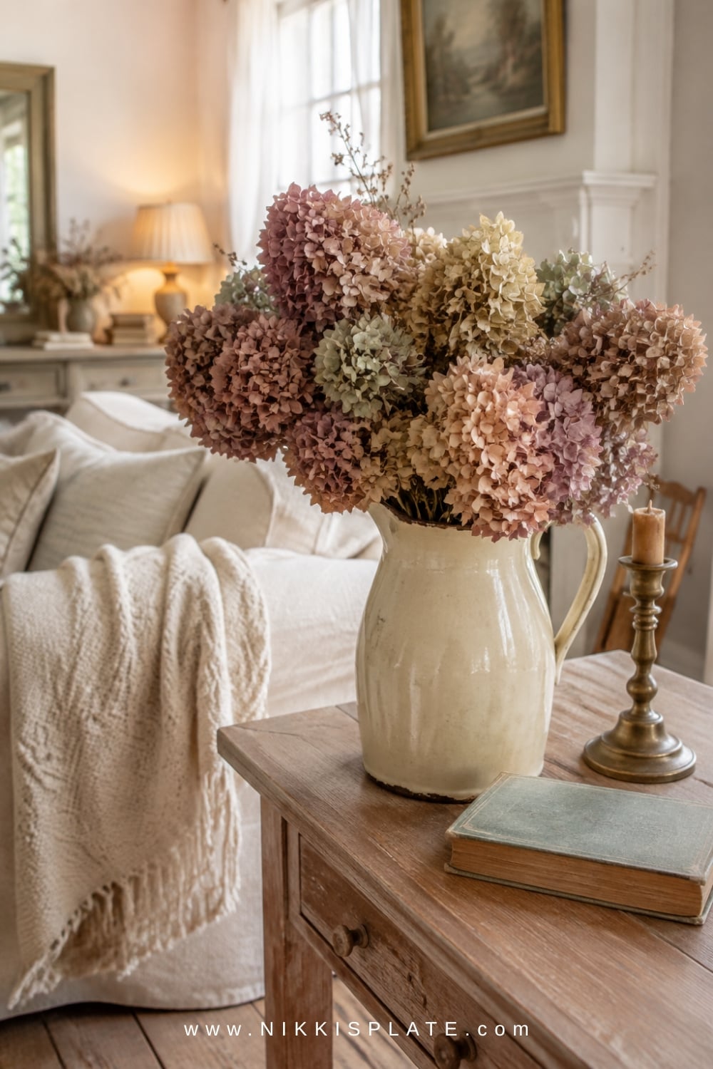 Loose dried hydrangeas in faded mauve, cream, green and brown arranged in an aged cream pitcher.