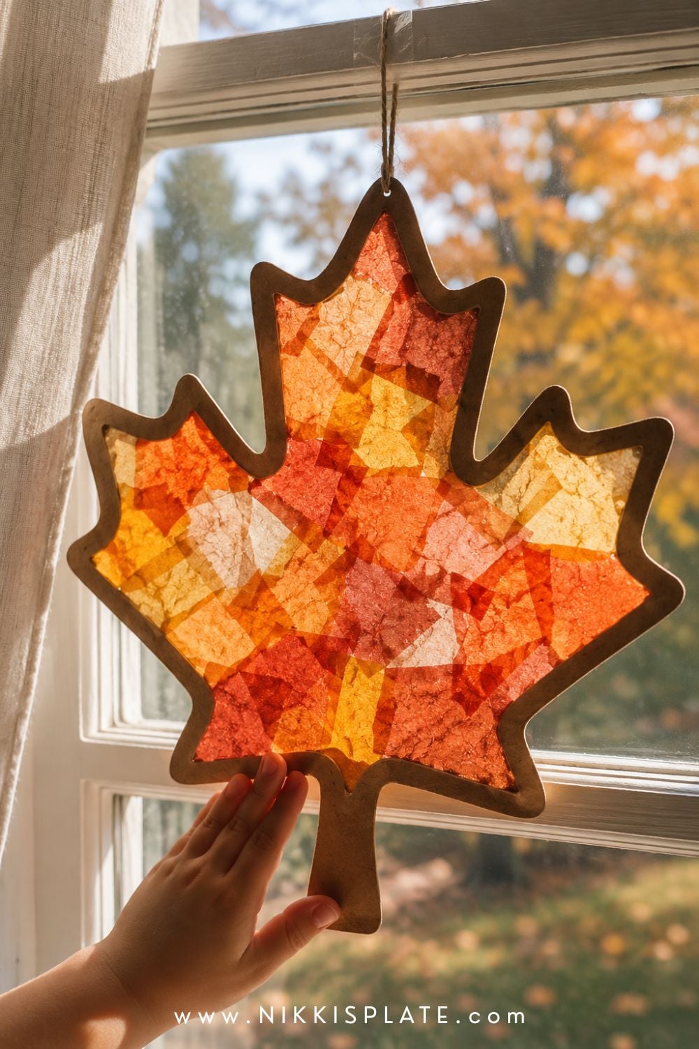 Printable fall leaf suncatcher filled with amber, rust and yellow tissue paper glowing in a sunny window.