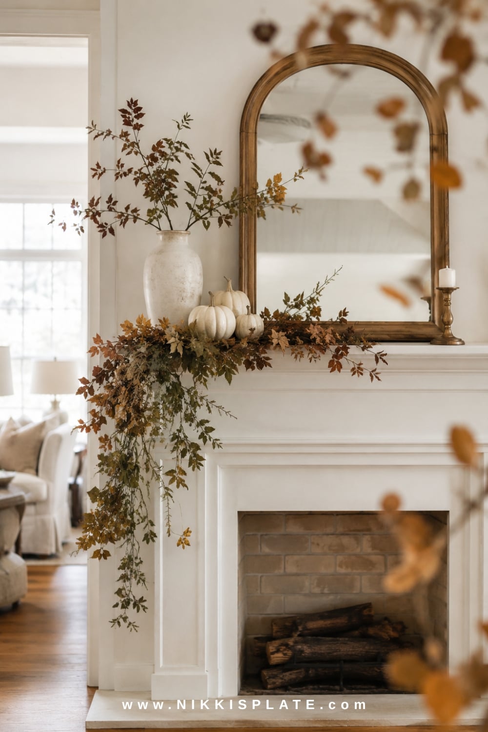 Asymmetrical fall mantel decor with cascading muted foliage, cream pumpkins, brass candlesticks and a vintage mirror.