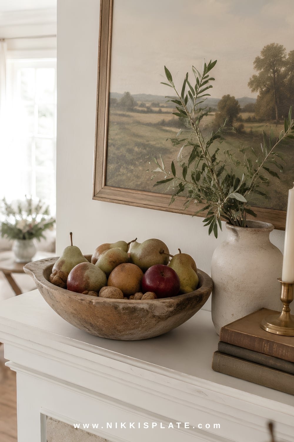 Rustic wood bowl filled with pears, apples and walnuts on a cozy fall mantel with vintage books and brass accents.