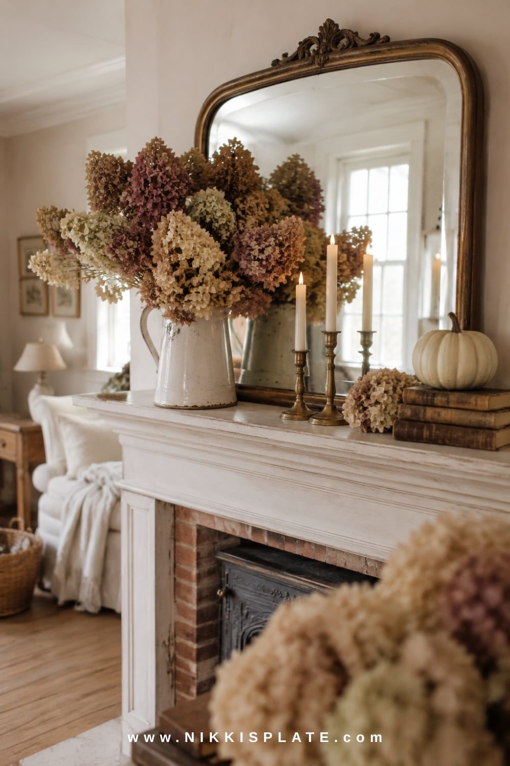 Romantic farmhouse fall mantel with dried hydrangeas, pale pumpkins, vintage books, brass candleholders and an antique-style mirror.