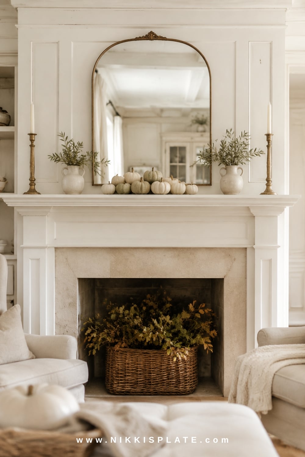 Elegant symmetrical fall mantel decor with an arched mirror, matching brass candlesticks, neutral pumpkins and balanced autumn branches.