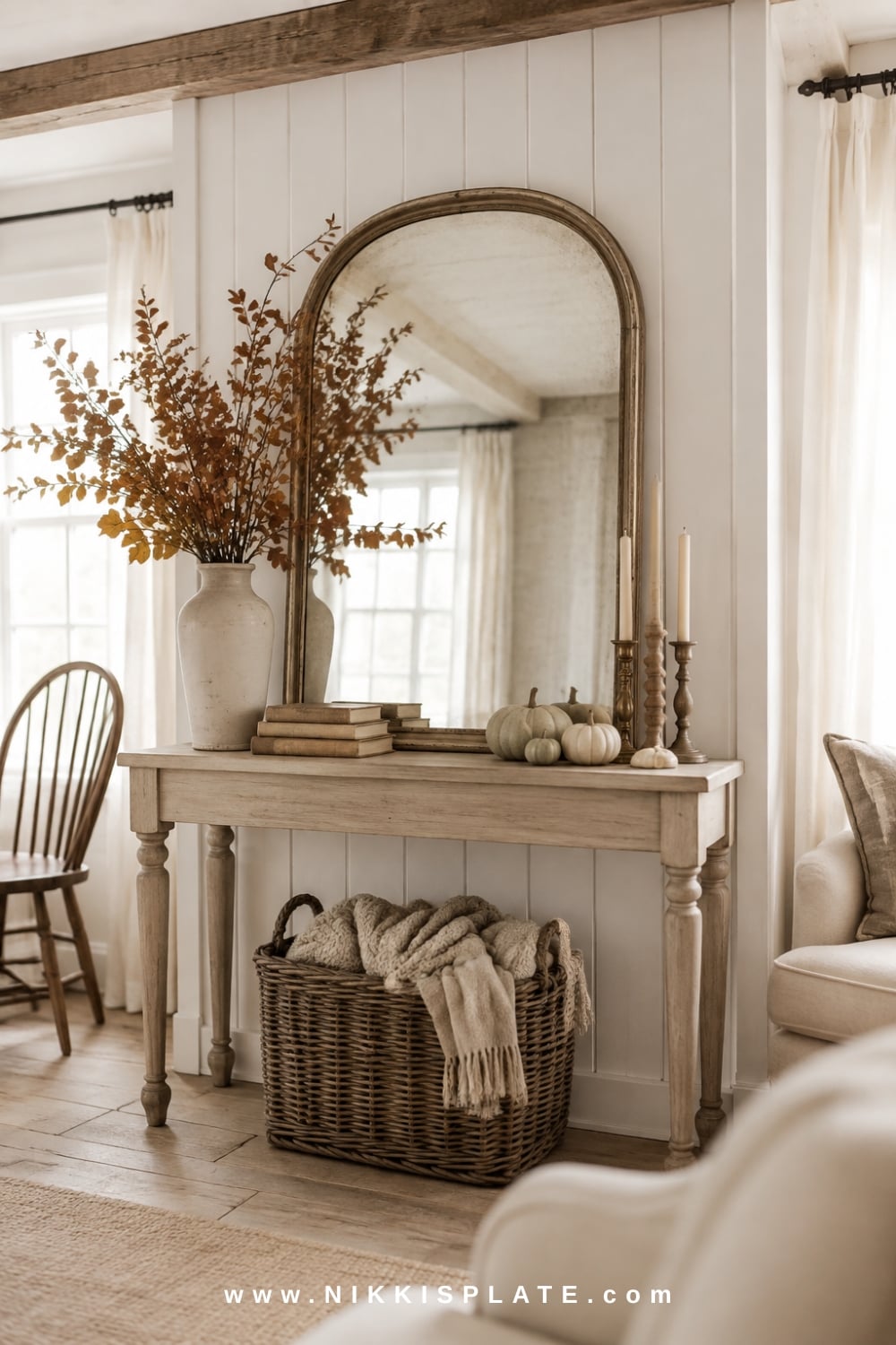 Faux fall mantel created on a white oak console with an arched mirror, muted branches, candlesticks, pumpkins and layered textiles.
