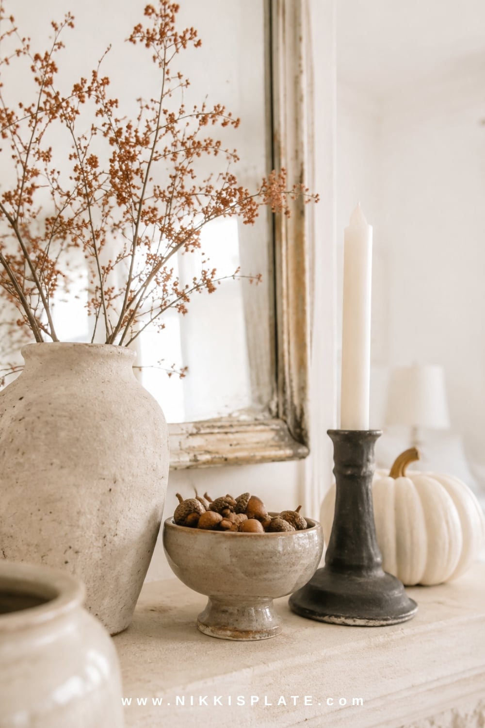 Handmade-looking cream, rust and charcoal pottery arranged with a pale pumpkin and aged mirror on a farmhouse fall mantel.
